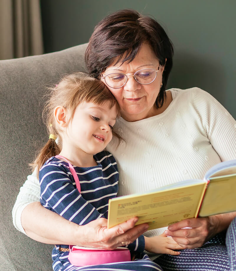 Grandmother reading a children’s book with her granddaughter at home.